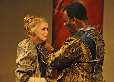 Othello has his hands around Desdemona's neck as she cries looking up at him. Both are dressed in ornate gold and black Renaissance outfits